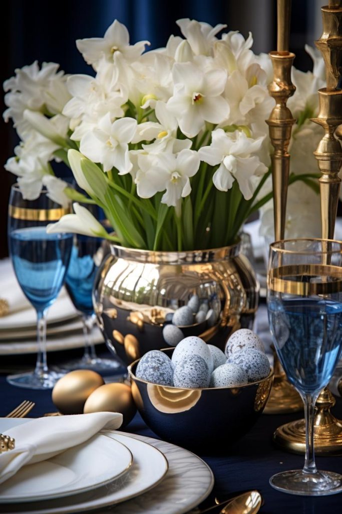 This blue table setting features a silver vase filled with daffodil flowers and decorated with gold eggs, and a metal bowl filled with blue <a href=