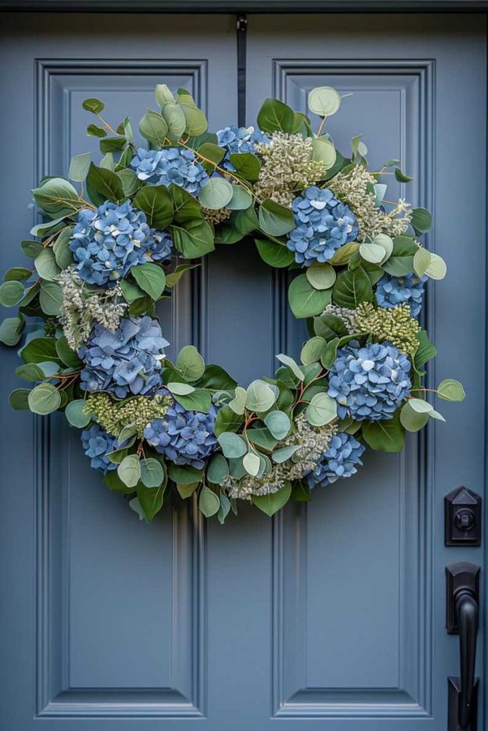 A blue door with a decorative wreath of blue hydrangeas and green leaves hanging on it.