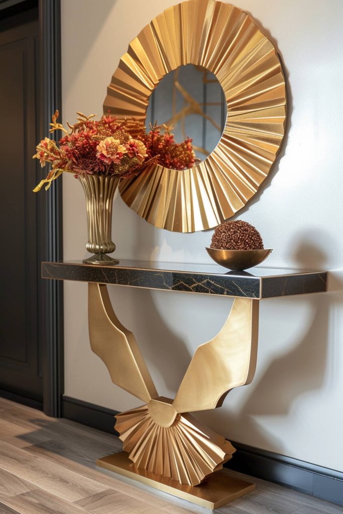 Gold console table with gold vase full of bright orange flowers and a gold sunburst mirror above