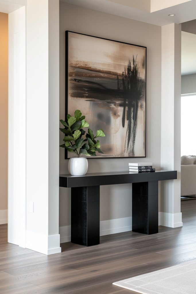 A black console table with a white vase full of green plants, a stack of books in black and white colors and above it an abstract painting with bold strokes