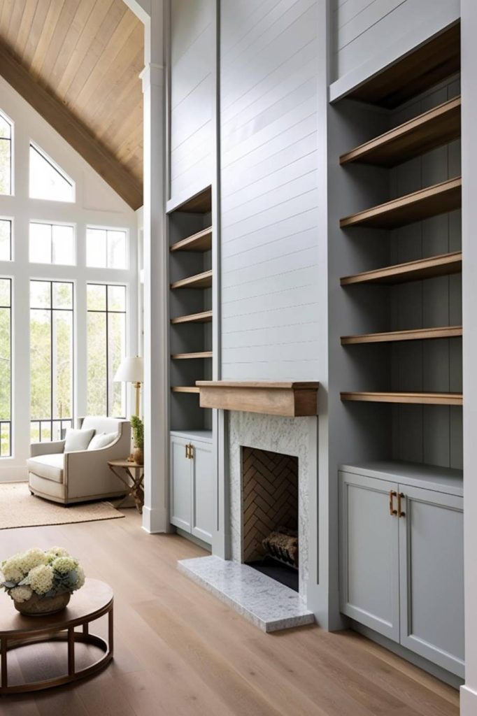 A modern living room with high ceilings, large windows, built-in shelves next to a fireplace and a cozy armchair next to a small round table with flowers.