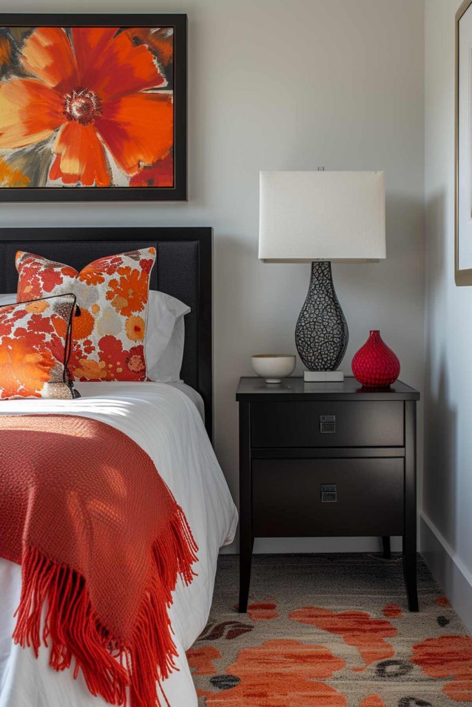 A black bedside table with a lamp with an ornate base and square lampshade, a decorative white ball and a red vase