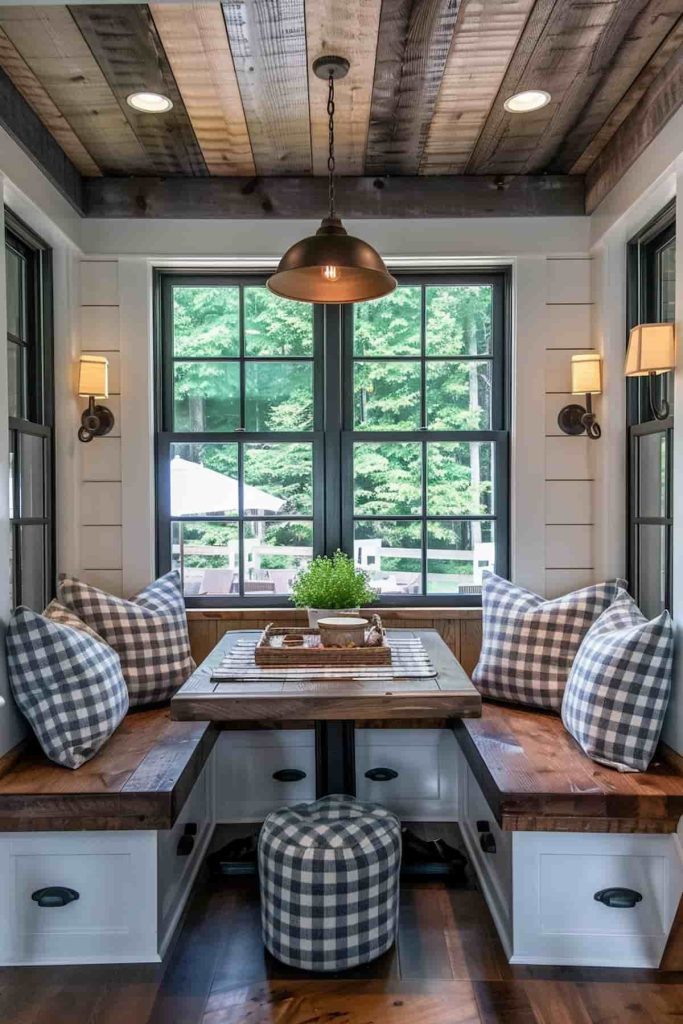 A cozy breakfast nook with a wooden table, built-in seating with checkered cushions, a ceiling lamp and windows overlooking the greenery.