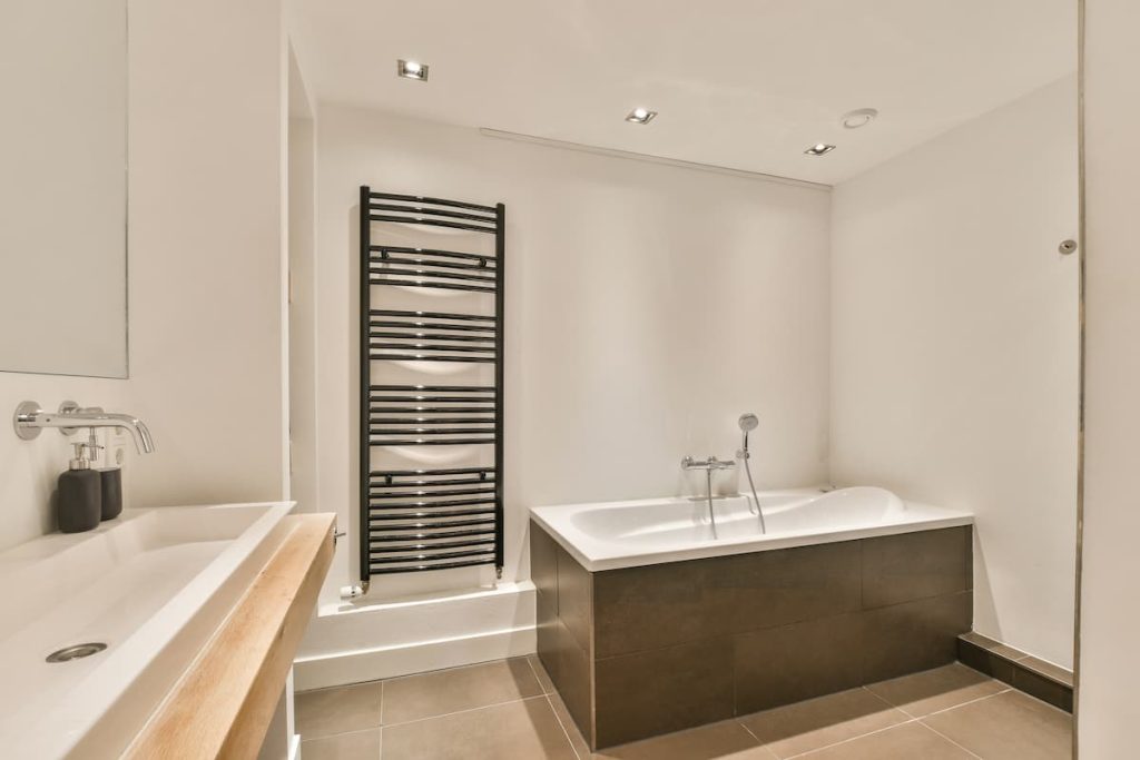 A bathroom with a bathtub, sink and towel rack in the middle of the room on the right