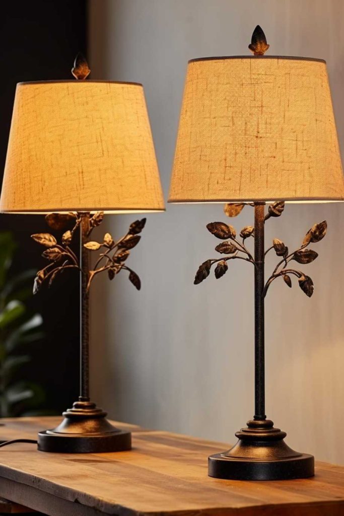 Two table lamps with beige shades and ornamental bases with leaf motifs stand side by side on a wooden surface.