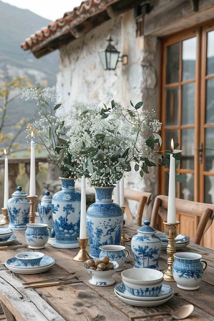 Outdoor table setting featuring blue and white ceramic paired with olive branches on a stone table and tapered white candles