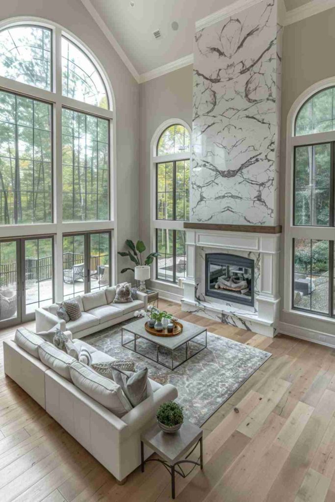 Spacious living room with high windows, a marble fireplace and light wooden floors. The modern decor includes a white cuttingof, a coffee table and a large inner plant on the side.