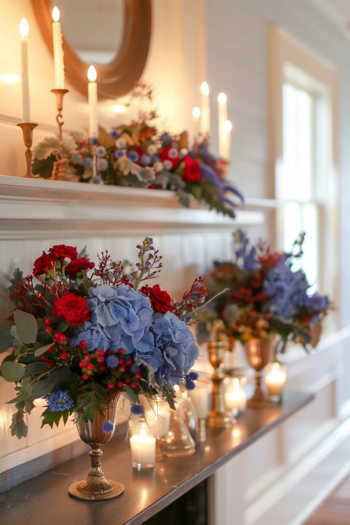 A fireplace that is adorned with elegant flower arrangements with red roses, blue hydrangeas and various green reasons. Candles in brass owners and glass votives are illuminated.